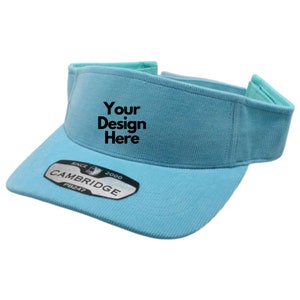 Puede incluir: Una visera azul claro con una etiqueta negra que dice "Your Design Here" y una etiqueta negra que dice "CAMBRIDGE SINCE 2000 PB247".