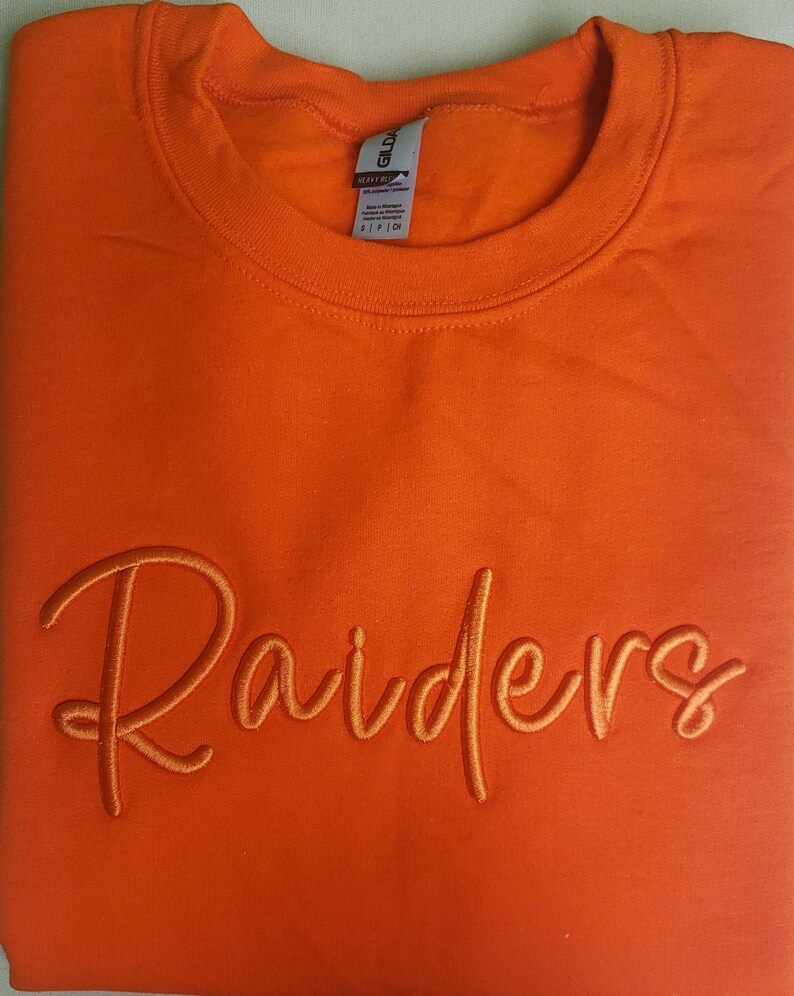 May include: Orange sweatshirt with the word "Raiders" embroidered in a cursive font.