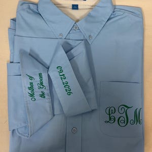 K&ouml;nnte beinhalten: Ein hellblaues Hemd mit Knopfleiste und Port Authority Etikett. Die Manschetten sind gr&uuml;n bestickt mit dem Text Mother of the Groom und 09.12.2026. Ein gr&uuml;nes Monogramm mit den Buchstaben LTM ist auf der Brusttasche aufgestickt.
