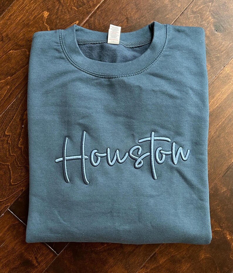 May include: A dark blue sweatshirt with the word "Houston" embroidered in a light blue cursive font.