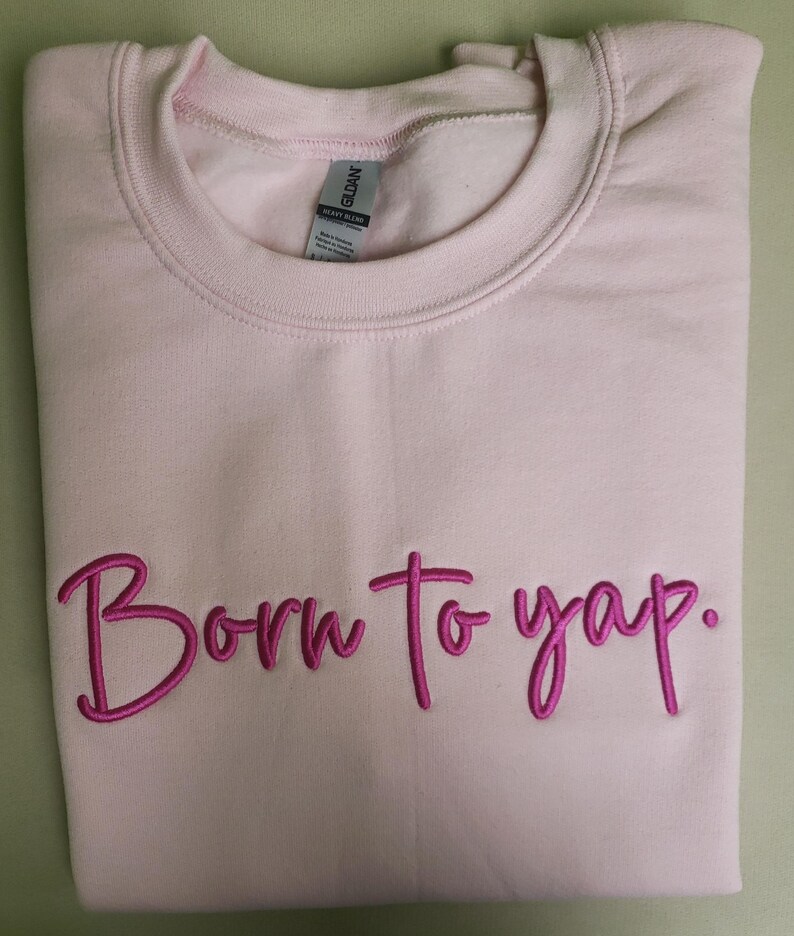May include: A pink sweatshirt with the phrase "Born to yap." embroidered in pink.