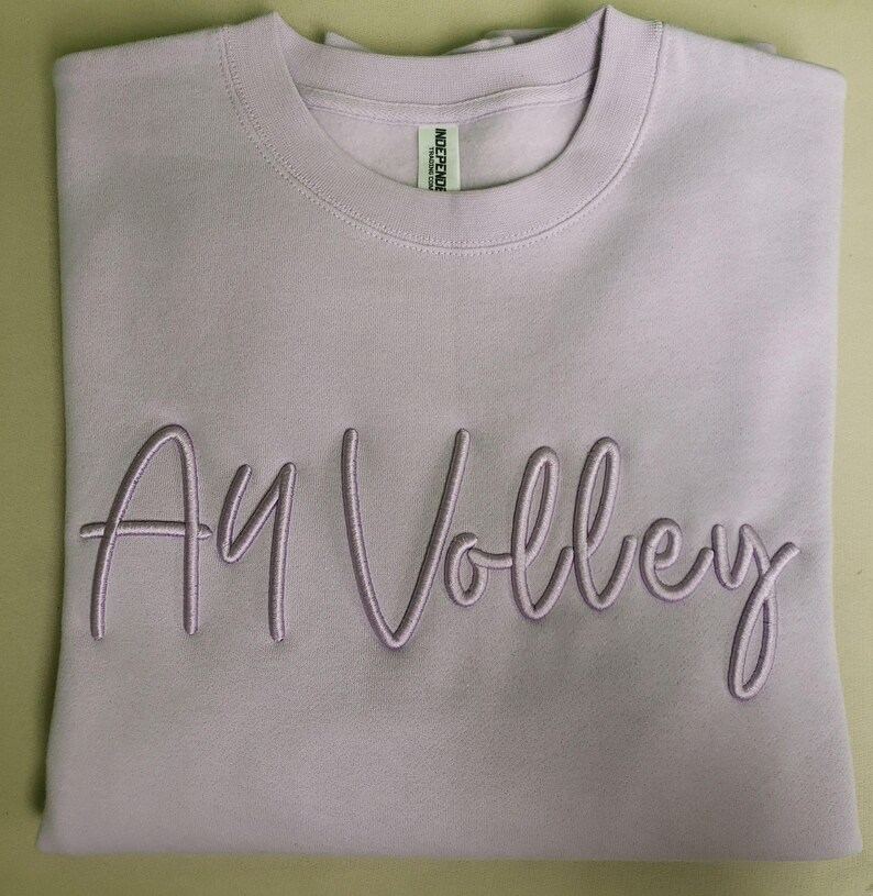 May include: A lavender sweatshirt with the text "Ay Volley" embroidered in a light purple colour.