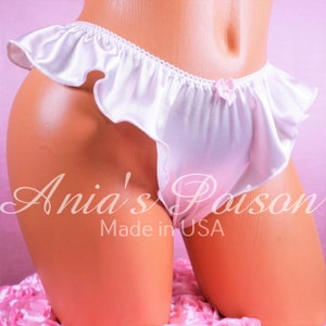 May include: White satin ruffled panties with a pink bow detail. The panties are made in the USA and have the text "Ania's Poison" printed on the front.