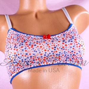 May include: A white bra with a red and blue star pattern. The bra has a white strap and a red bow at the center. The bra has a blue trim and the words "Made in USA" are printed on the bottom.