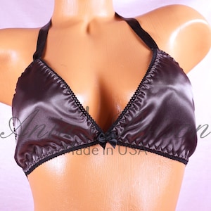 May include: A dark gray satin halter bra with black trim and a small bow at the center. The bra has a delicate, feminine design with a smooth, shiny texture. The bra is made in the USA.