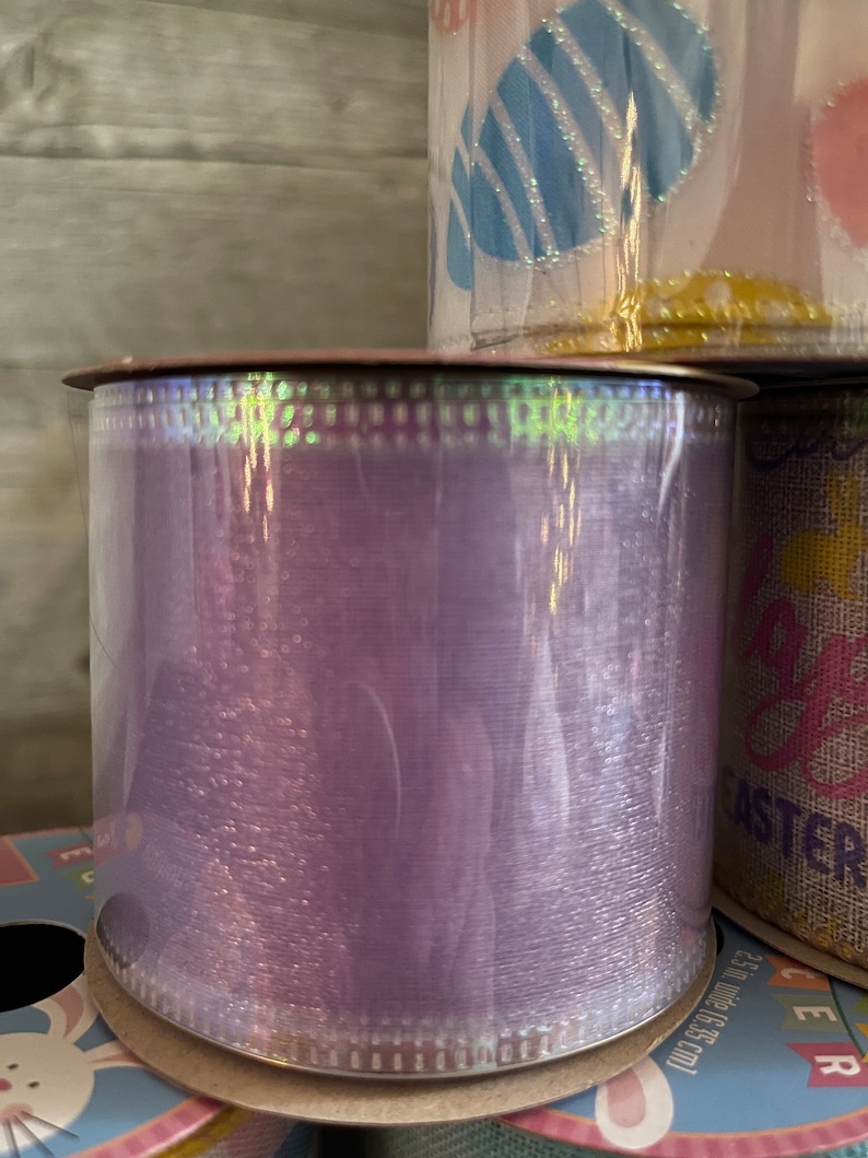 K&ouml;nnte beinhalten: Eine Rolle schimmerndes violettes Band mit wei&szlig;em gepunktetem Rand. Das Band ist um einen Pappzylinder gewickelt.