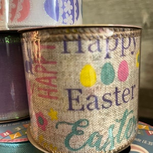 K&ouml;nnte beinhalten: Eine Rolle aus Juteband mit beigefarbenem Hintergrund und einem sich wiederholenden Muster aus bunten Ostereiern und dem Text "Frohe Ostern".