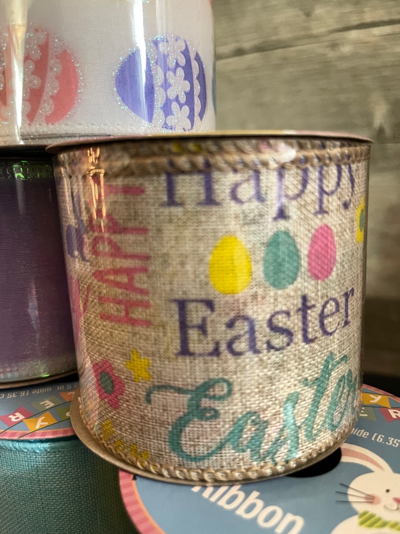 K&ouml;nnte beinhalten: Eine Rolle aus Juteband mit beigefarbenem Hintergrund und einem sich wiederholenden Muster aus bunten Ostereiern und dem Text "Frohe Ostern".
