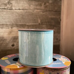 K&ouml;nnte beinhalten: Drei Rollen Band mit Ostern-Motiven. Die obere Rolle ist hellblau, die mittlere Rolle hat ein kariertes Muster in Pink, Blau und Gelb, und die untere Rolle hat einen braunen Jute-Hintergrund mit einem wei&szlig;en Hasen und dem aufgedruckten Text "Frohe Ostern".