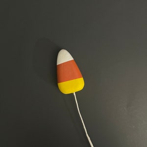 May include: A white, orange, and yellow candy corn shaped ornament with a white string attached.