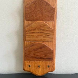 May include: Wooden mail organizer with three pockets and three key hooks. The organizer is made of light brown wood with a natural grain. The top has a decorative, curved edge. The key hooks are small, brass-colored knobs.