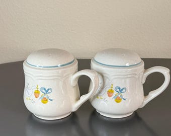 May include: A pair of off-white ceramic salt and pepper shakers with a speckled finish. Each shaker features a handle, a blue rim on the lid, and a graphic print of a white goose holding a yellow strawberry with a blue ribbon and bow.