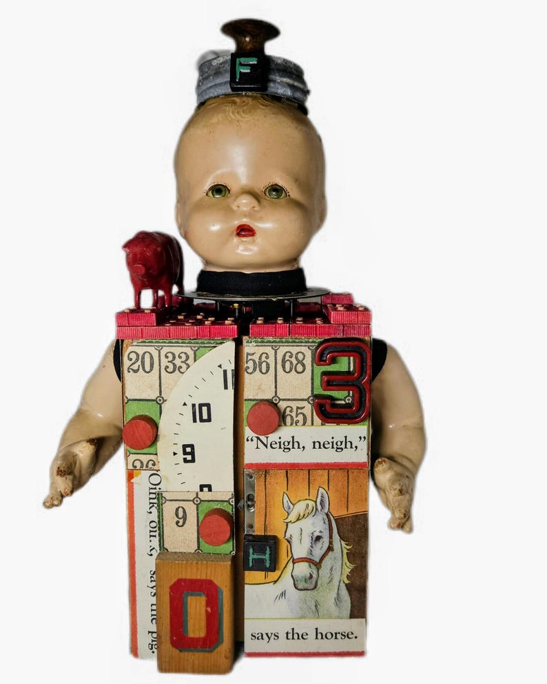 May include: A mixed-media doll sculpture featuring a vintage doll head topped with a gray cap and letter F, a red pig figurine, and a rectangular body constructed from blocks, bingo cards, a clock face, and a horse illustration with the text Neigh, neigh, says the horse.