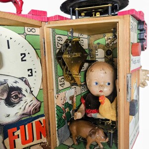 May include: A mixed-media assemblage art piece featuring a wooden box structure with a clock face, a pig figurine, and an interior compartment containing a vintage doll, a small chicken figurine, a brown pig figurine, and exposed brass clockwork gears.