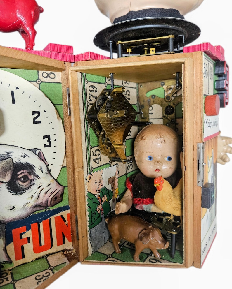 May include: A mixed-media assemblage art piece featuring a wooden box structure with a clock face, a pig figurine, and an interior compartment containing a vintage doll, a small chicken figurine, a brown pig figurine, and exposed brass clockwork gears.