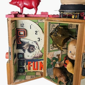 May include: A wooden box assemblage art piece featuring a red plastic pig on top, a clock face with a pig illustration, the letter P, the word FUN, and black letter blocks. Inside, a doll head, a small brown pig, and a chicken figurine are visible.