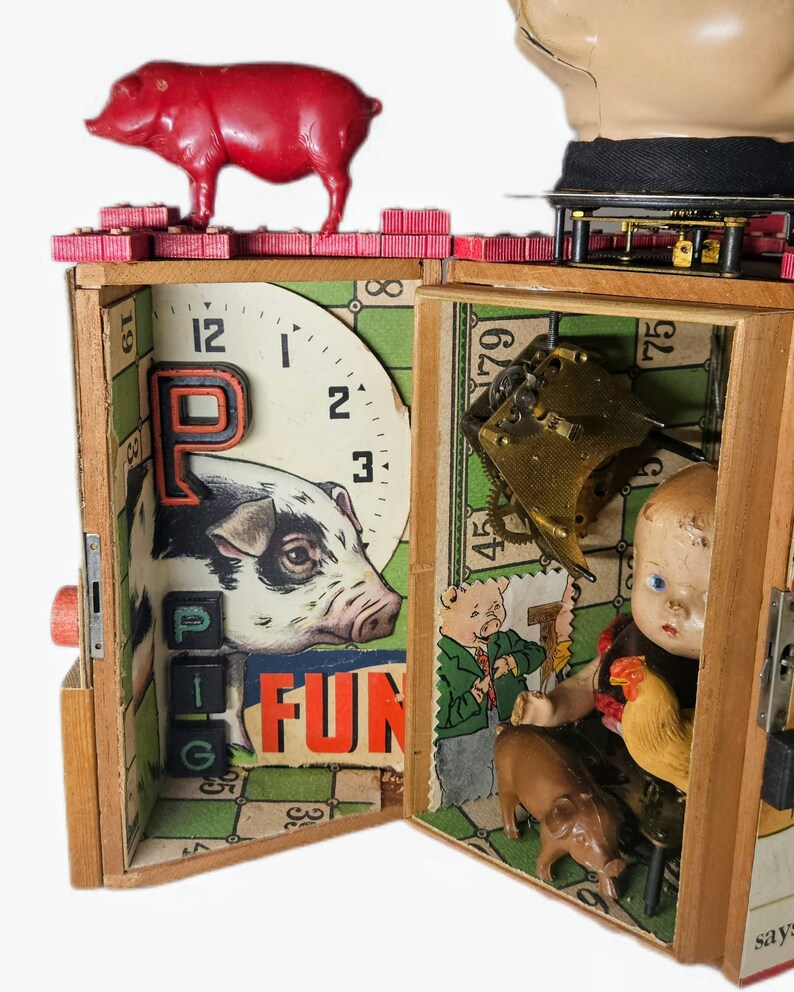 May include: A wooden box assemblage art piece featuring a red plastic pig on top, a clock face with a pig illustration, the letter P, the word FUN, and black letter blocks. Inside, a doll head, a small brown pig, and a chicken figurine are visible.