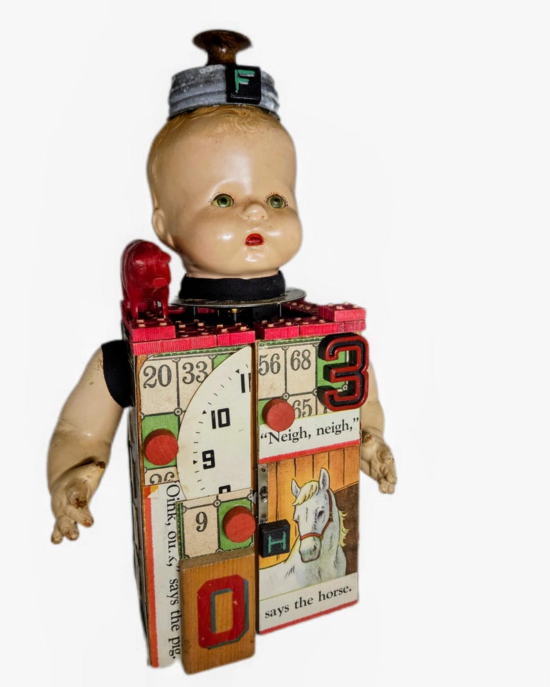 May include: A mixed-media doll sculpture featuring a vintage plastic doll head topped with a metal lid and the letter F. The rectangular body is constructed from wooden blocks decorated with bingo cards, a horse illustration, and the text "Neigh, neigh," says the horse and "Oink, ou," says the pig. It includes a small red pig figurine, the number 3, the number 0, and red wooden circles.