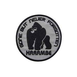 Könnte beinhalten: Ein runder, grauer gestickter Aufnäher mit einer schwarzen Gorilla-Silhouette. Der Text um den Gorilla lautet "Gone But Never Forgotten" und der Text unter dem Gorilla lautet "Harambe".