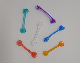 May include: Six plastic clasps in various colors, including blue, purple, orange, and white. The clasps are all in the shape of a simple loop with a small knob on one end.