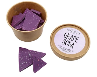 May include: A brown paper cup filled with purple soy wax melts with glitter. The cup is next to a round brown container with a white label that reads "RUSTIC SUGAR CREEK CO. GRAPE SODA SOY WAX MELTS MADE IN UTAH DO NOT EAT".