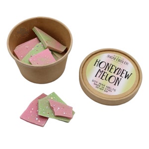 May include: A brown paper container filled with pink and green soy wax melts. The container is labeled "Honeydew Melon" with the text "Soy Wax Melts Made in Utah Do Not Eat" on the label.