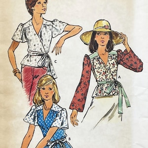 Op de afbeelding: Illustratie van drie wikkel tops met verschillende bloemen- en stippenpatronen. Eén top heeft rode mouwen met een bloemenmotief, een andere heeft korte mouwen en de derde heeft een blauw stippenpatroon. Elke top heeft een striksluiting.