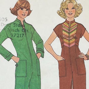 以下が含まれることがあります： 2つのジャンプスーツのイラスト。1つは緑色で「Drug Store Beach Ctr. 97217」の文字が入っています。もう1つは茶色で、胴体にカラフルなシェブロン柄があります。どちらもポケットとジッパーが付いています。