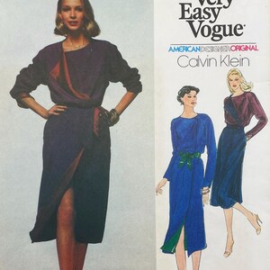 Puede incluir: Un patrón de costura Very Easy Vogue de Calvin Klein que presenta un vestido cruzado con mangas largas y un lazo lateral. El sobre del patrón muestra una fotografía de un modelo con un vestido morado oscuro e ilustraciones en azul y morado.
