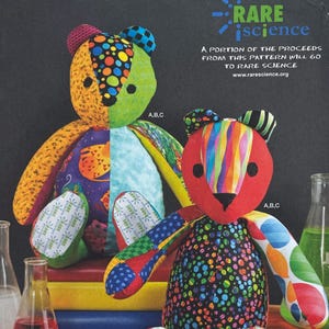 Può includere: Due orsacchiotti patchwork colorati. Uno ha la faccia verde e arancione, l'altro rossa. Gli orsi sono fatti di vari tessuti fantasia, tra cui pois e righe. Il testo "RARE science" e un messaggio di beneficenza sono visibili.