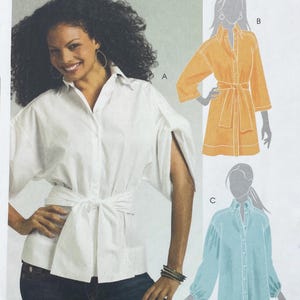 May include: A sewing pattern illustration featuring three shirt variations. Version A is a white button-down shirt with wide sleeves and a tie waist. Version B is a yellow button-down shirt with a tie waist. Version C is a light blue button-down shirt.