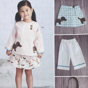 May include: A young girl wearing a pink and white gingham top and skirt set with brown dog appliqués. The skirt features a dog print. Additional images show a blue and white checkered skirt with dog appliqués and white pants with blue trim.