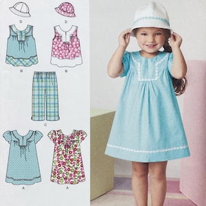 May include: A sewing pattern envelope featuring illustrations of a short-sleeved dress, pants, and a bucket hat in various floral and plaid prints. The image displays technical line drawings alongside a photograph of a child wearing the blue dress.