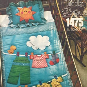 Könnte beinhalten: Little Vogue 1475 Schnittmuster mit einer blauen Steppdecke und einem Sonnenkissen. Die Decke zeigt eine Wäscheleine mit applizierten grünen Latzhosen mit der Aufschrift Jonathan, einem roten gemusterten Hemd mit der Aufschrift January 1 1977, einer Socke und einem gelben Hemd sowie einer weißen Wolke.