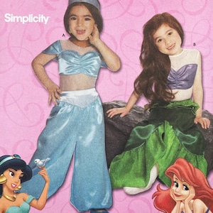 May include: A Simplicity sewing pattern envelope featuring two costumes. Costume A is a light blue two-piece outfit with a cropped top and wide-leg pants. Costume B is a mermaid-style outfit with a purple top and a long green skirt with ruffles.
