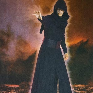 May include: A person in a black hooded robe with a wide black belt and a red accent. The person is gesturing with their right hand, with a blurred, fiery background.