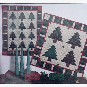 Peut inclure: Deux tentures murales matelassées avec des motifs de sapins de Noël verts et rouges, présentées avec trois grands arbres décoratifs bleu sarcelle et deux wagons de train miniatures, un rouge et un vert, sur une surface sombre.