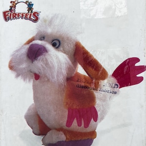 Op de afbeelding: Een Firffels knuffel met een wit en oranje lichaam, een paarse neus en een kleine rode tong. Het wezen heeft lange oranje oren, roze vleugelachtige aanhangsels aan de zijkanten en een roze staart. Het Firffels-logo is linksboven zichtbaar.