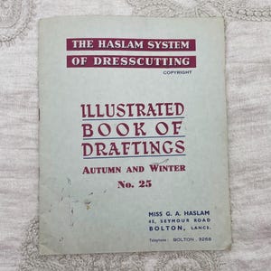 May include: A light gray softcover book titled The Haslam System of Dresscutting, Illustrated Book of Draftings, Autumn and Winter No. 25. The cover features dark red and blue text, including the address Miss G. A. Haslam, 45, Seymour Road, Bolton, Lancs.