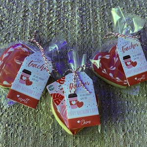 May include: Three heart-shaped cookies decorated with white swirls and a red glaze. Each cookie is packaged in a clear plastic bag with a gift tag that reads "If you've got a teacher who's probably wants lots of coffee... Happy Valentine's Day". The tags are signed with the names "Wyatt", "Aven", and "Wyatt".