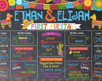 May include: A chalkboard style first birthday sign for twins named Ethan and Elijah. The sign is decorated with colorful Mexican fiesta decorations. It includes details about their height, weight, first words, and favorite foods. The sign also lists their favorite songs and activities.