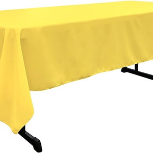 May include: A bright yellow rectangular tablecloth draped over a table. The tablecloth has a smooth, wrinkle-free surface.
