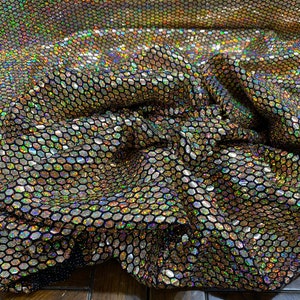 May include: Black fabric with a holographic iridescent honeycomb pattern. The fabric is wrinkled and has a shiny, metallic finish.