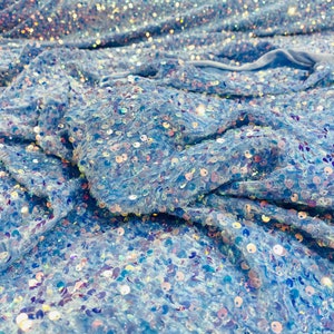 Puede incluir: Paillettes iridiscentes azules sobre una tela transparente. Las lentejuelas están dispersas aleatoriamente sobre la tela, creando un efecto brillante.