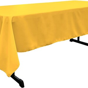 May include: A bright yellow rectangular tablecloth. The tablecloth is draped over a table and has a smooth, even texture.