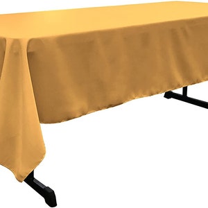 May include: A gold rectangular tablecloth with a smooth, silky texture. The tablecloth is draped over a table with black metal legs.