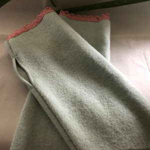 May include: A pair of light blue arm warmers with pink lace trim. The arm warmers have a seam down the side and a pocket on the inside.