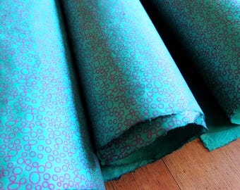 Puede incluir: Tres rollos de papel turquesa vibrante con un patrón repetitivo de círculos y óvalos de color morado oscuro dibujados a mano. El papel tiene una apariencia fibrosa y texturizada con bordes irregulares visibles en los extremos de las hojas.