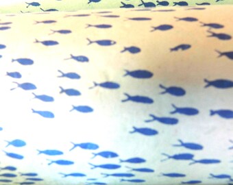 Puede incluir: Un objeto cilíndrico con una superficie de color crema claro que presenta un patrón repetitivo de pequeñas siluetas de peces de color azul oscuro orientadas en varias direcciones por toda el área visible del material.