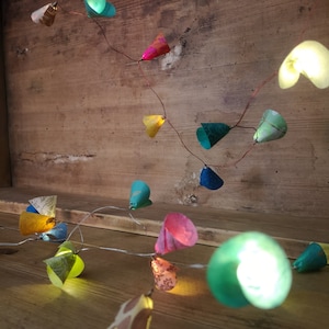 Puede incluir: Una cadena de luces con coloridos papeles en forma de cono. Las luces est&aacute;n enhebradas en un alambre de cobre y est&aacute;n encendidas, proyectando un brillo c&aacute;lido. Los papeles son de varios colores, incluyendo verde, azul, rosa, amarillo y naranja.